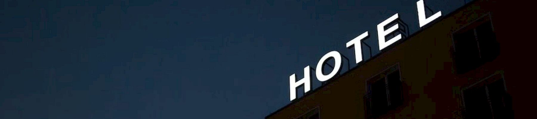 A hotel building with the illuminated word &ldquo;HOTEL&rdquo; on top against a dark blue sky.
