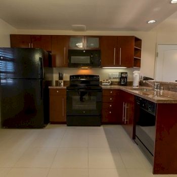 A modern L-shaped kitchen with dark wood cabinets, black appliances (refrigerator, oven, microwave, dishwasher), a tile floor, and a breakfast bar corner.