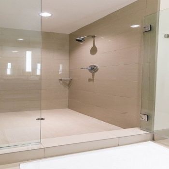 A modern glass-enclosed walk-in shower with beige tile walls, a rainfall showerhead, a handheld sprayer, and a separate bench area. End.