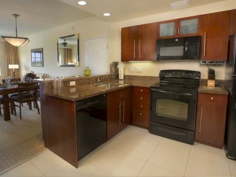 A modern U-shaped kitchen with dark wood cabinets, black appliances, a center island, and a view into the dining area, all well-lit.