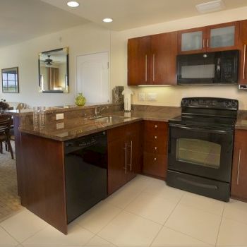 A modern kitchen with dark wood cabinets, black appliances, a granite island, and a connected dining area in the background, bright and neat.