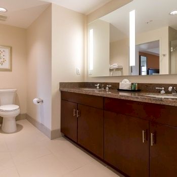 A modern bathroom with a granite double-sink vanity and a separate toilet in a bright, clean suite.