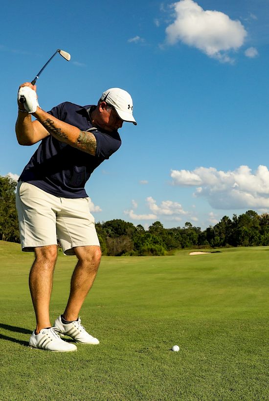 A golfer swings a club on a sunny green fairway under a blue sky with fluffy clouds.