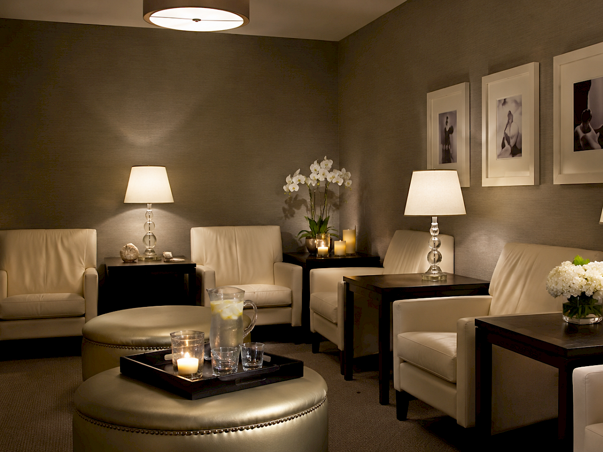 A cozy, neutral lounge with cream armchairs, side tables, lamps, flower arrangements, and framed photos on the wall.