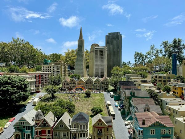 A miniature cityscape with colorful row houses in the foreground and taller modern buildings rising behind, under a blue, sunny sky.