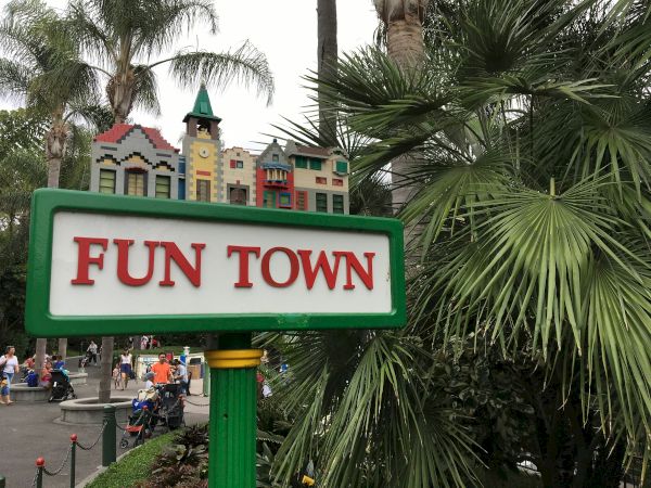 A bright &ldquo;FUN TOWN&rdquo; sign with colorful little buildings atop a green post, surrounded by lush palm trees and park-like scenery.