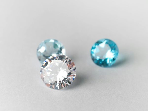 Three small gemstones&mdash;one clear diamond and two blue stones&mdash;rest on a light surface, catching soft light as they sparkle beautifully.