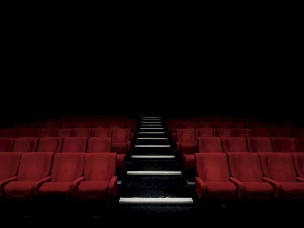 An empty red theater with lit steps leading to a dark stage, rows of seats fading into the distance, awaiting a performance.