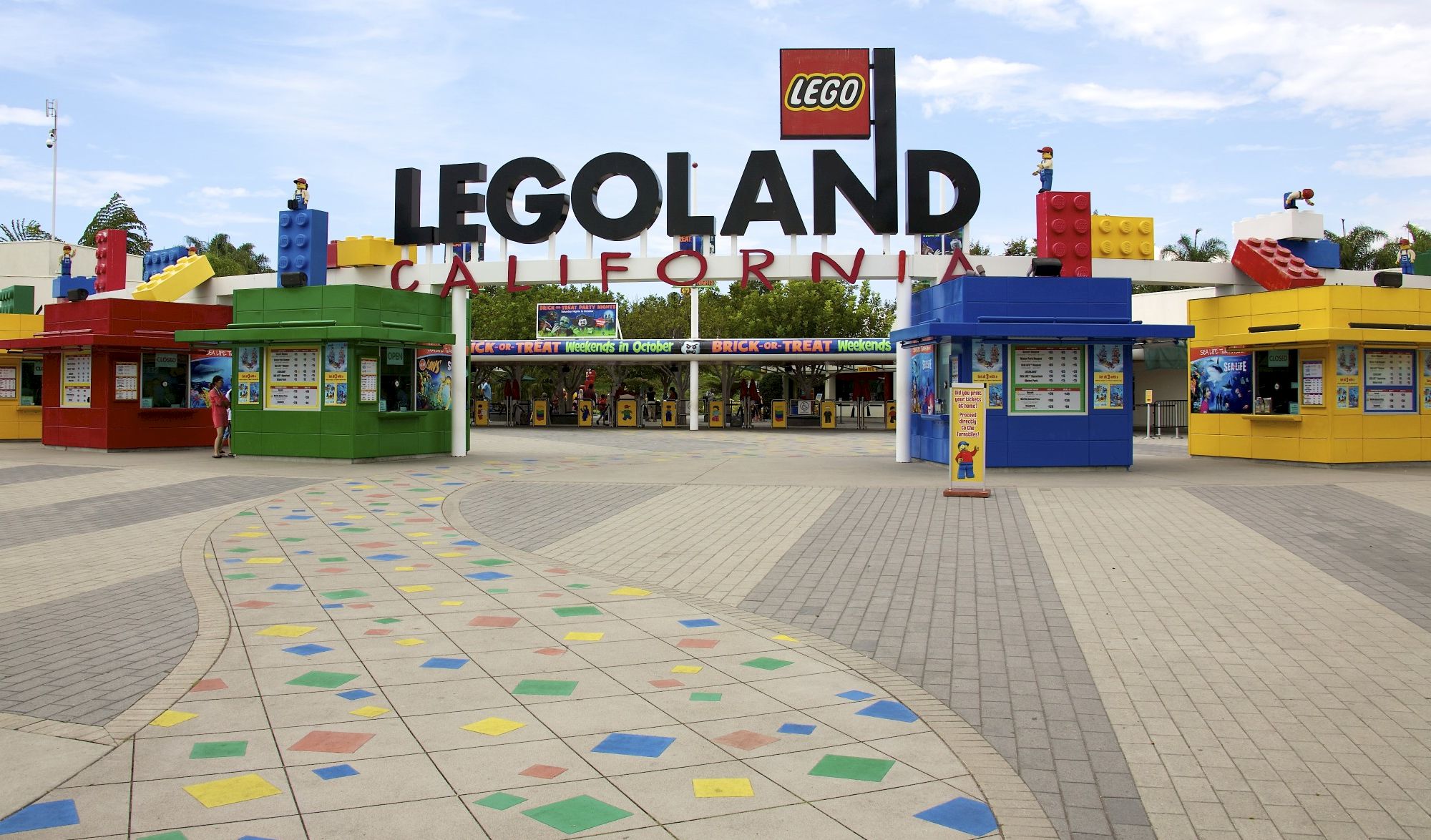 A LEGO Land entrance with giant LEGO letters, colorful blocks, and minifigure statues under a blue sky.