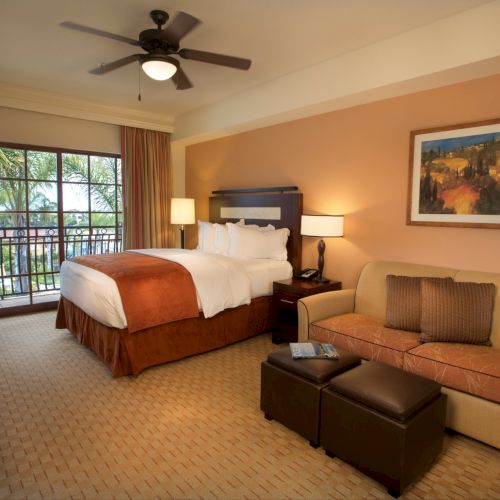A hotel bedroom with a king-size bed, ceiling fan light, seating area, and large window doors opening to greenery.