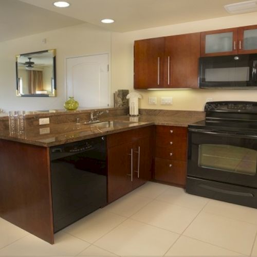 Spacious home kitchen with granite island, dark wood cabinets, built-in oven and microwave, plus a refrigerator and nearby dining area.