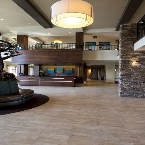 A hotel-style lobby with stone walls, tiled floor, a front desk, and modern lighting and seating.